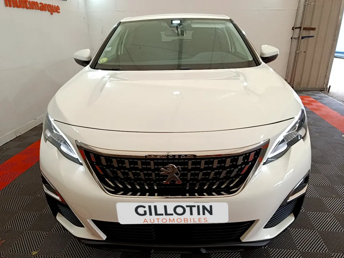 Vue frontale d'un Peugeot 3008 blanc avec calandre noire et phares LED allumés en intérieur showroom.