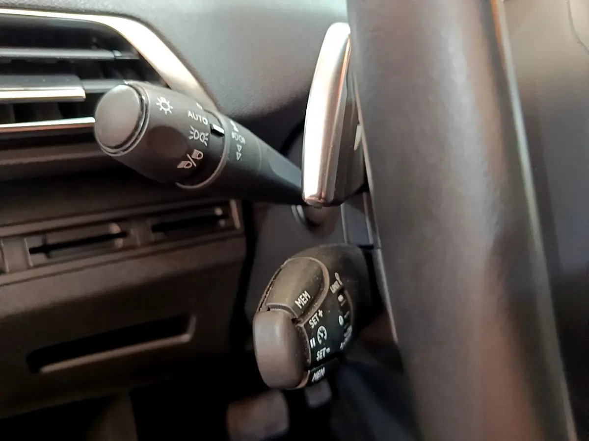 Gros plan sur les commandes au volant côté gauche d’un Peugeot 3008 blanc, montrant les réglages du régulateur de vitesse.