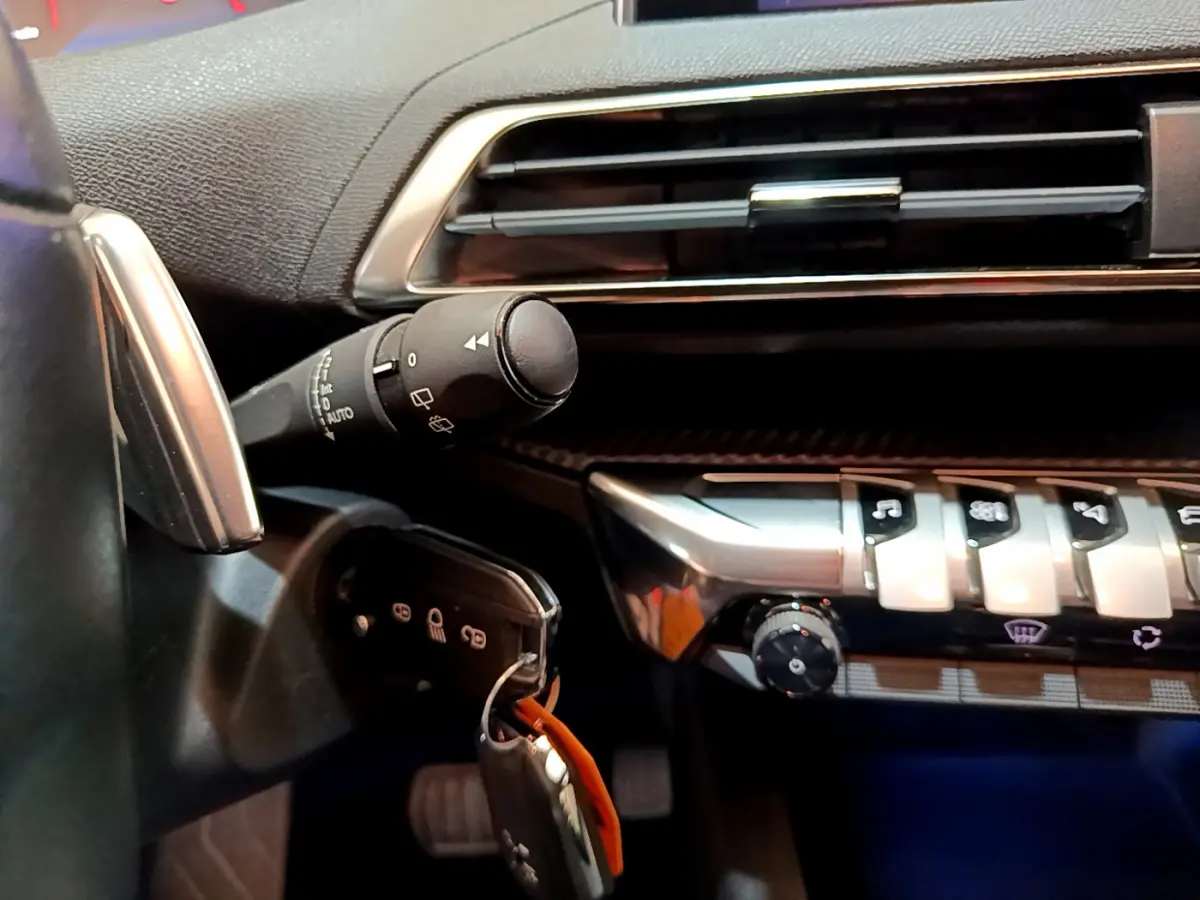 Gros plan sur la partie gauche du tableau de bord noir du Peugeot 3008 blanc, avec commandes et clé insérée.