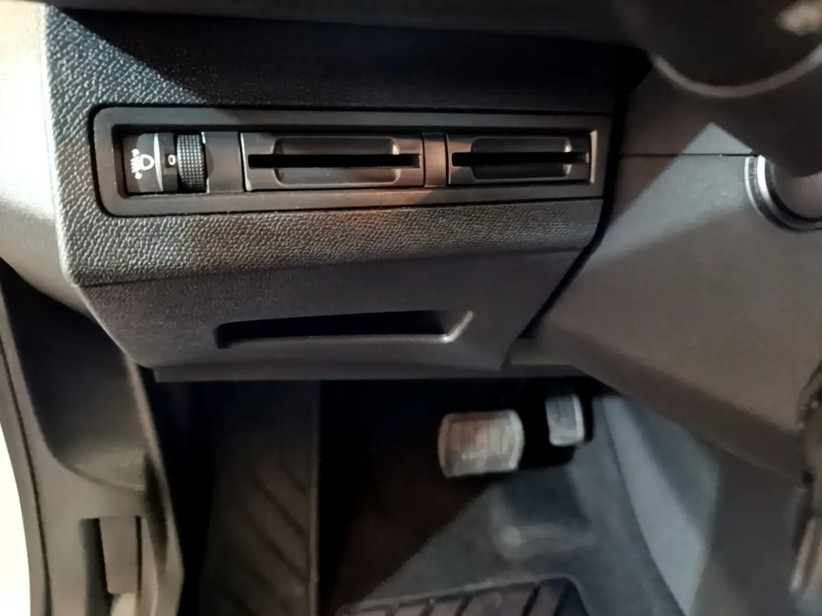 Vue rapprochée des commandes d'éclairage et des pédales côté conducteur dans l'habitacle noir du Peugeot 3008 blanc 2020.