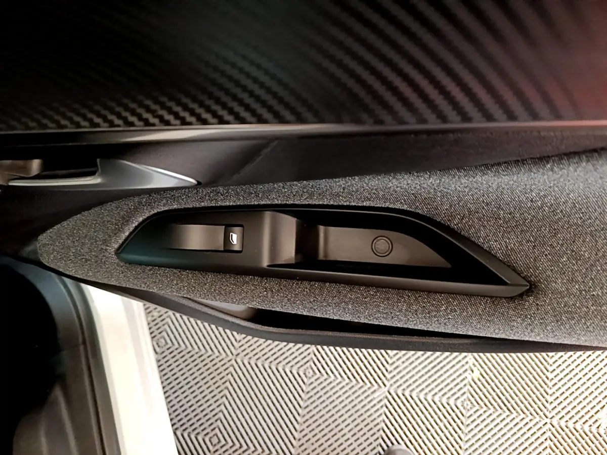 Gros plan sur la commande de lève-vitre côté conducteur, avec garniture tissu gris et poignée argentée du Peugeot 3008 blanc.