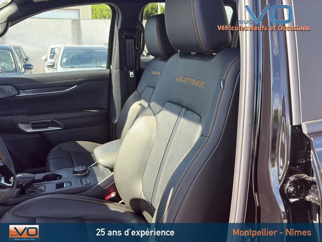 Intérieur noir du Ford Ranger Wildtrak 2025 en vue latérale, sièges avant en cuir avec surpiqûres orange visibles.