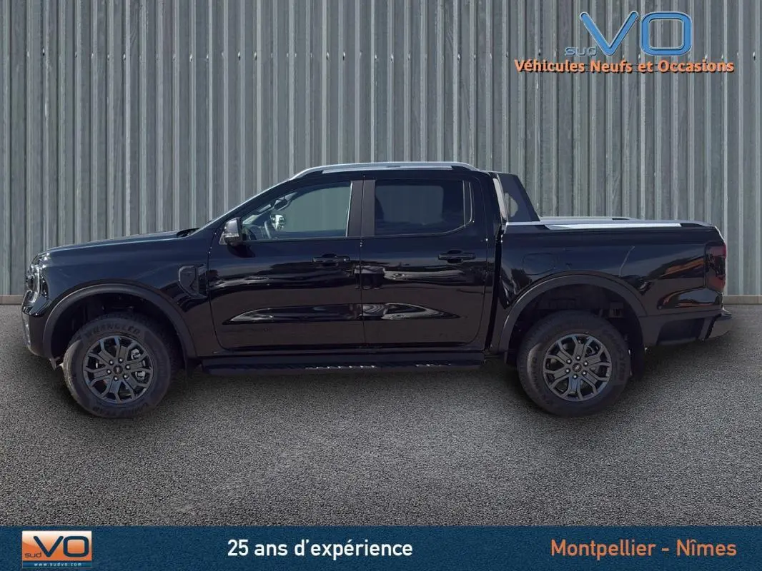 Profil latéral gauche du Ford Ranger noir double cabine avec jantes alliage 18 pouces et barres de toit visibles.