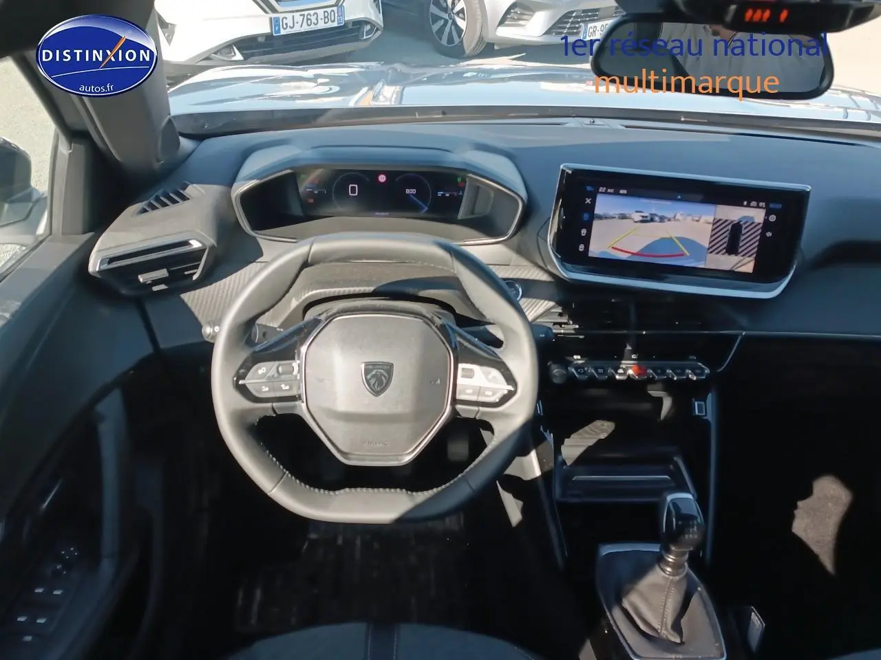 Vue intérieure frontale du poste de conduite du Peugeot 2008 gris, avec volant multifonction et écran tactile affichant la caméra de recul.