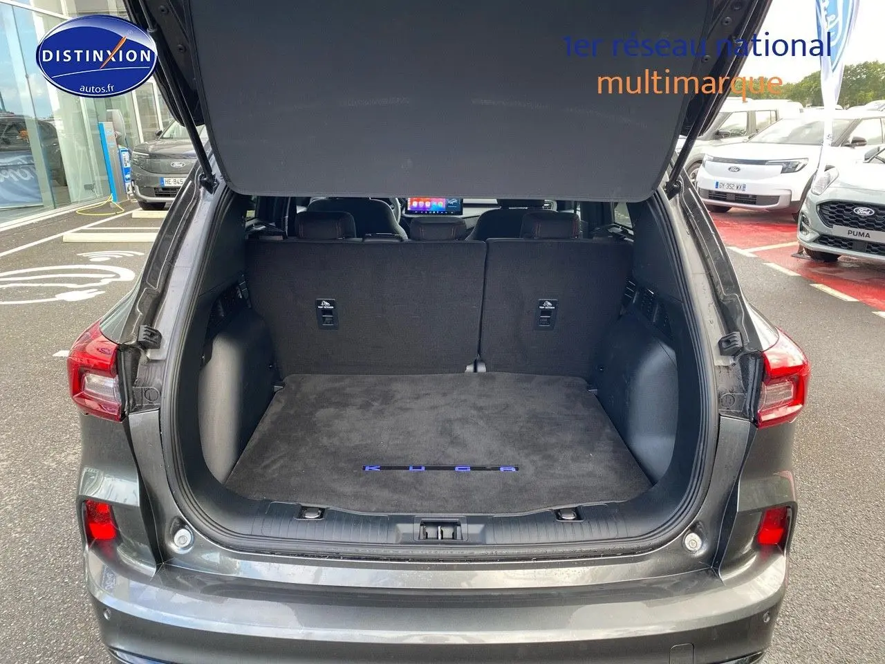 Vue arrière du Ford Kuga gris Magnetic avec coffre ouvert et tapis de coffre marqué KUGA visible.