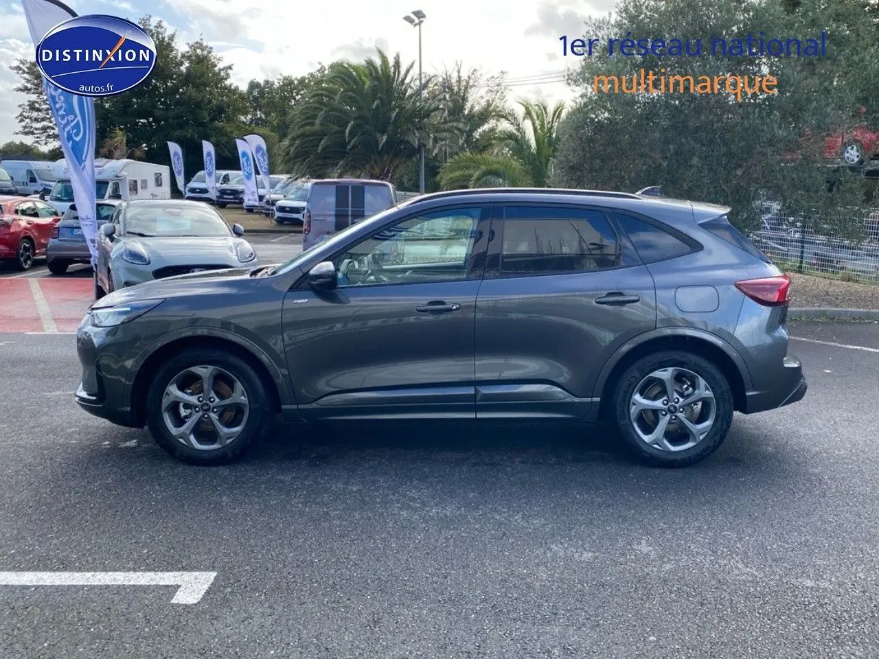 Vue de profil côté gauche d'un Ford Kuga 2025 gris métallisé garé en extérieur sur un parking.