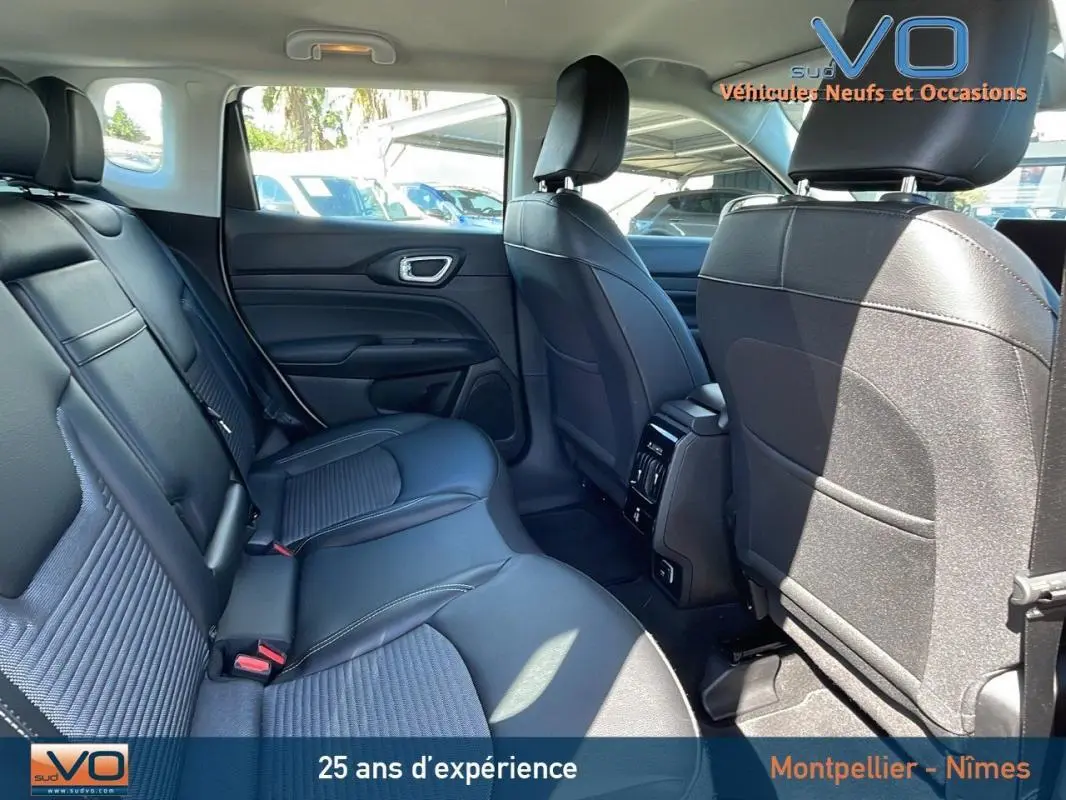 Vue intérieure arrière du Jeep Compass 2024 blanc, sièges noirs en cuir avec accoudoir central et prises USB visibles.