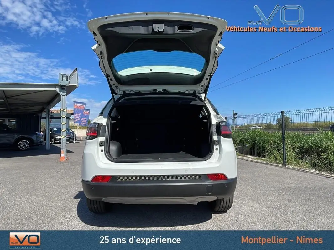 Vue arrière d'un Jeep Compass blanc 2024 avec coffre ouvert sur un parking ensoleillé