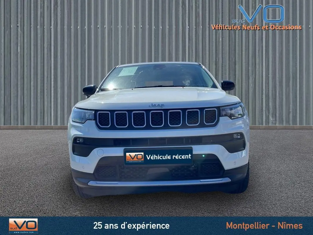 Vue frontale d'un Jeep Compass blanc 2024 avec calandre distinctive et phares LED allumés sur fond neutre.