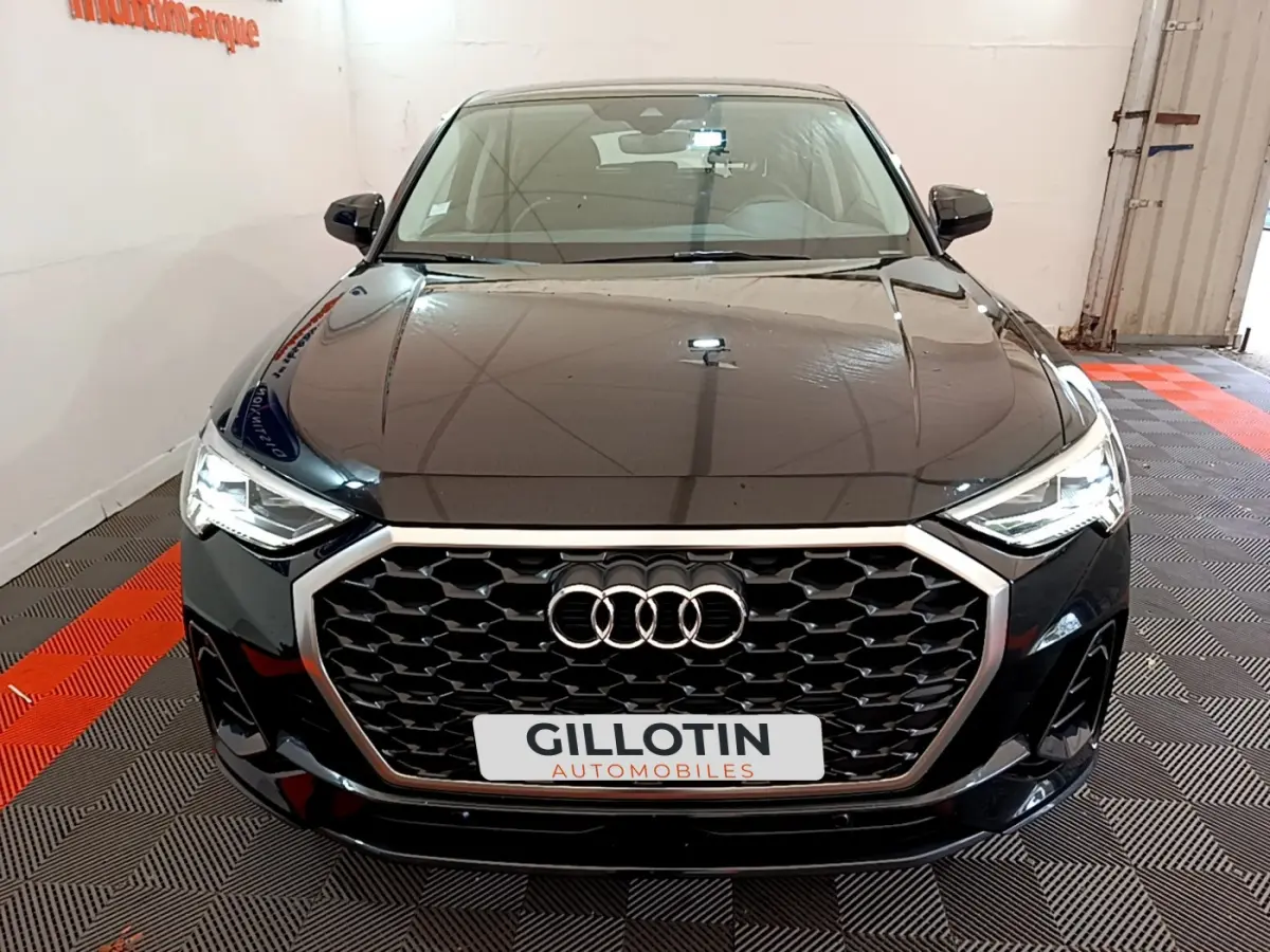 Audi Q3 Sportback noir vue de face mettant en valeur sa calandre hexagonale et ses phares LED allumés.