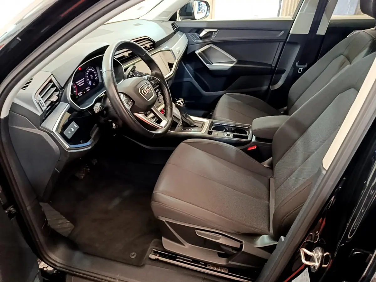 Intérieur côté conducteur d'Audi Q3 Sportback noir 2021, volant cuir, tableau de bord digital et sièges tissu gris.