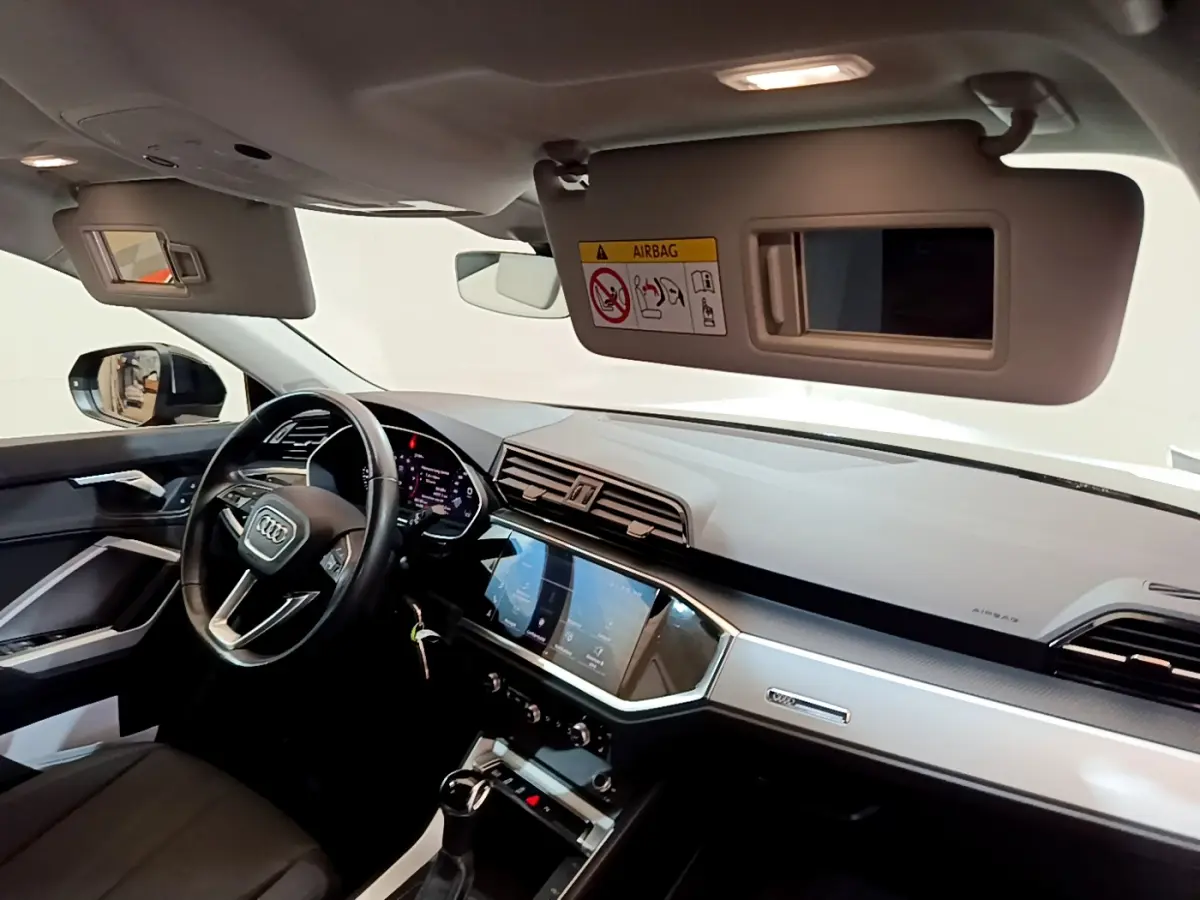 Intérieur de l'Audi Q3 Sportback 2021 vu côté conducteur, tableau de bord moderne avec écran tactile et volant cuir noir.
