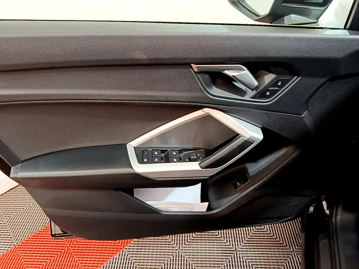 Vue intérieure côté gauche de la porte d'une Audi Q3 Sportback 2021 noire, avec commandes électriques et poignée argentée.