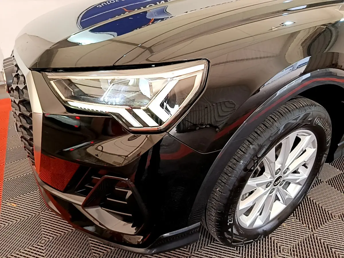 Gros plan sur l'avant droit noir brillant de l'Audi Q3 Sportback 2021, mettant en valeur son phare LED et la roue.