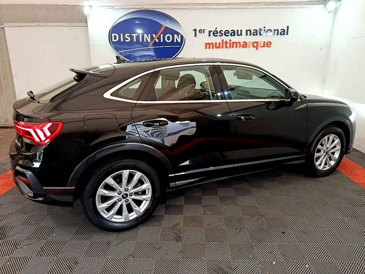 Audi Q3 Sportback noir vu de profil côté gauche, avec feux arrière LED allumés dans un showroom.