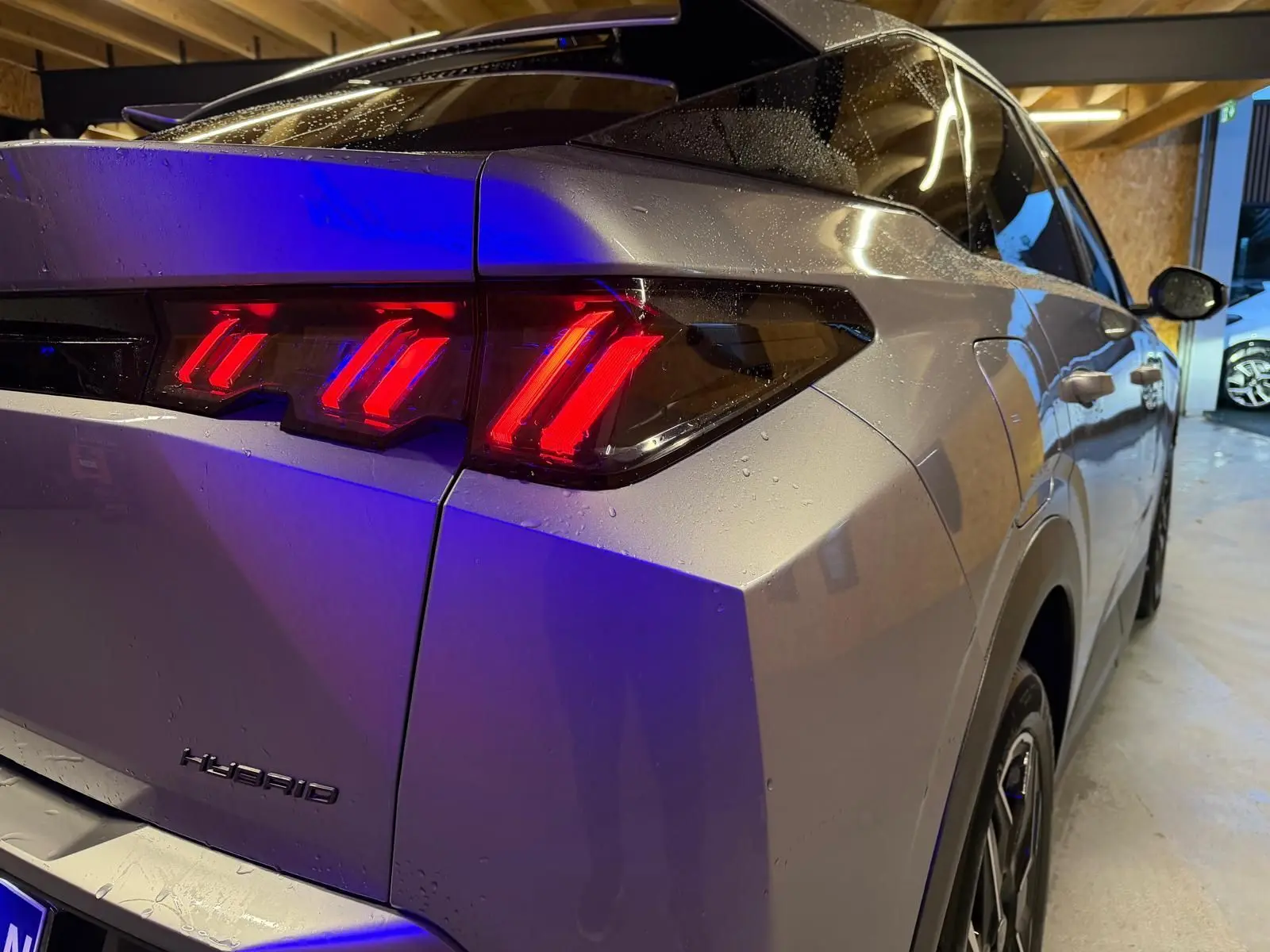 Vue 3/4 arrière droit du Peugeot 3008 gris 2025, mettant en valeur les feux arrière LED rouges et l'inscription Hybrid.