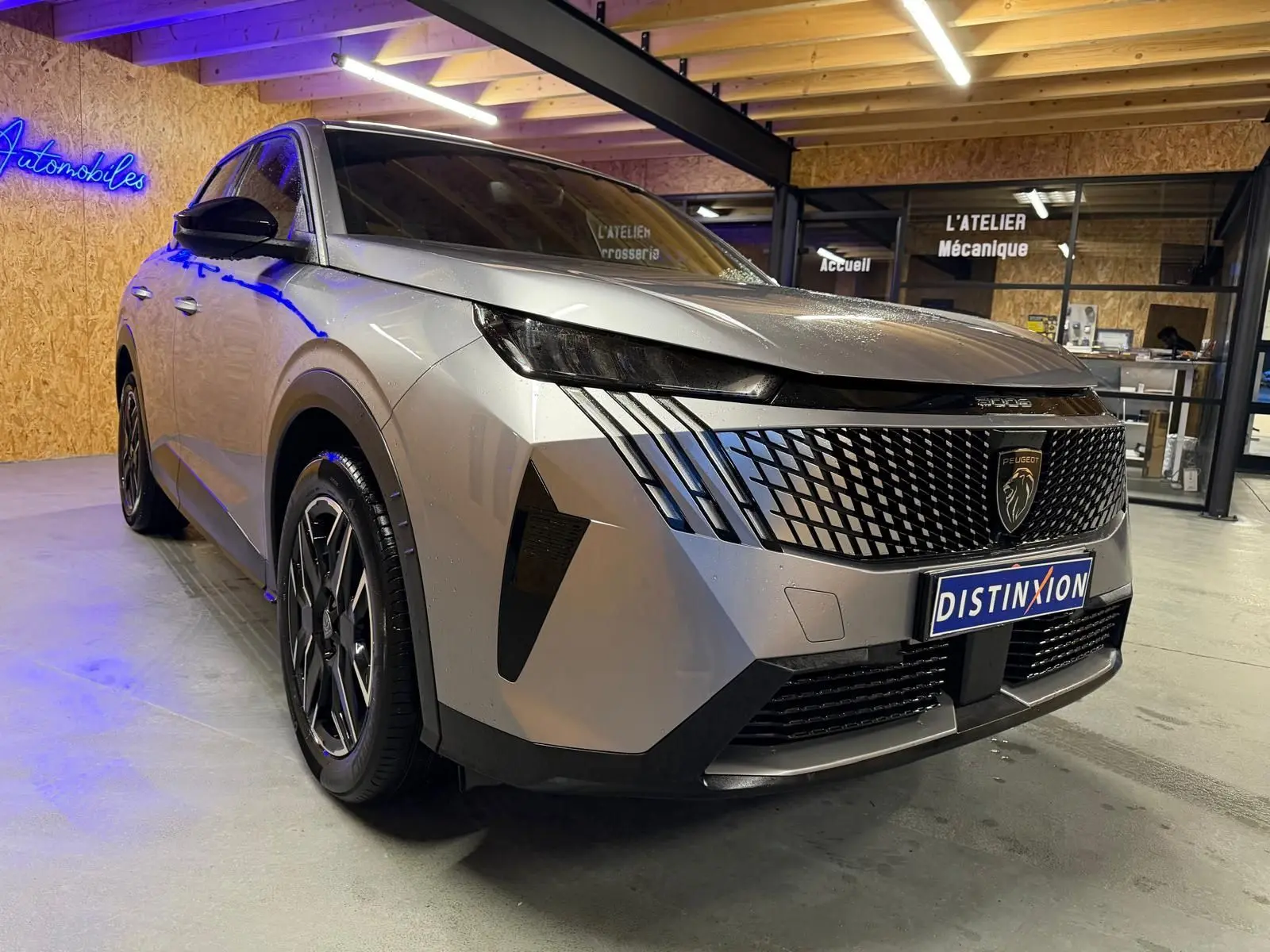 Vue 3/4 avant droit d'un Peugeot 3008 gris 2025 avec calandre noire et signature lumineuse distinctive en intérieur d'atelier.