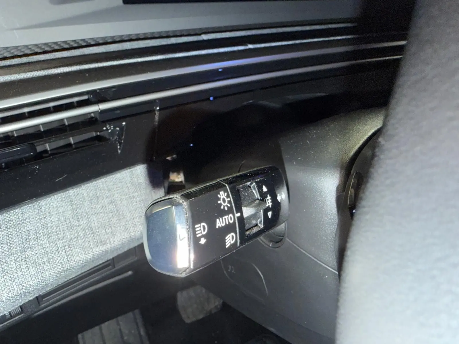 Gros plan sur la commande des phares à gauche du volant dans l’habitacle noir du Peugeot 3008 gris 2025.