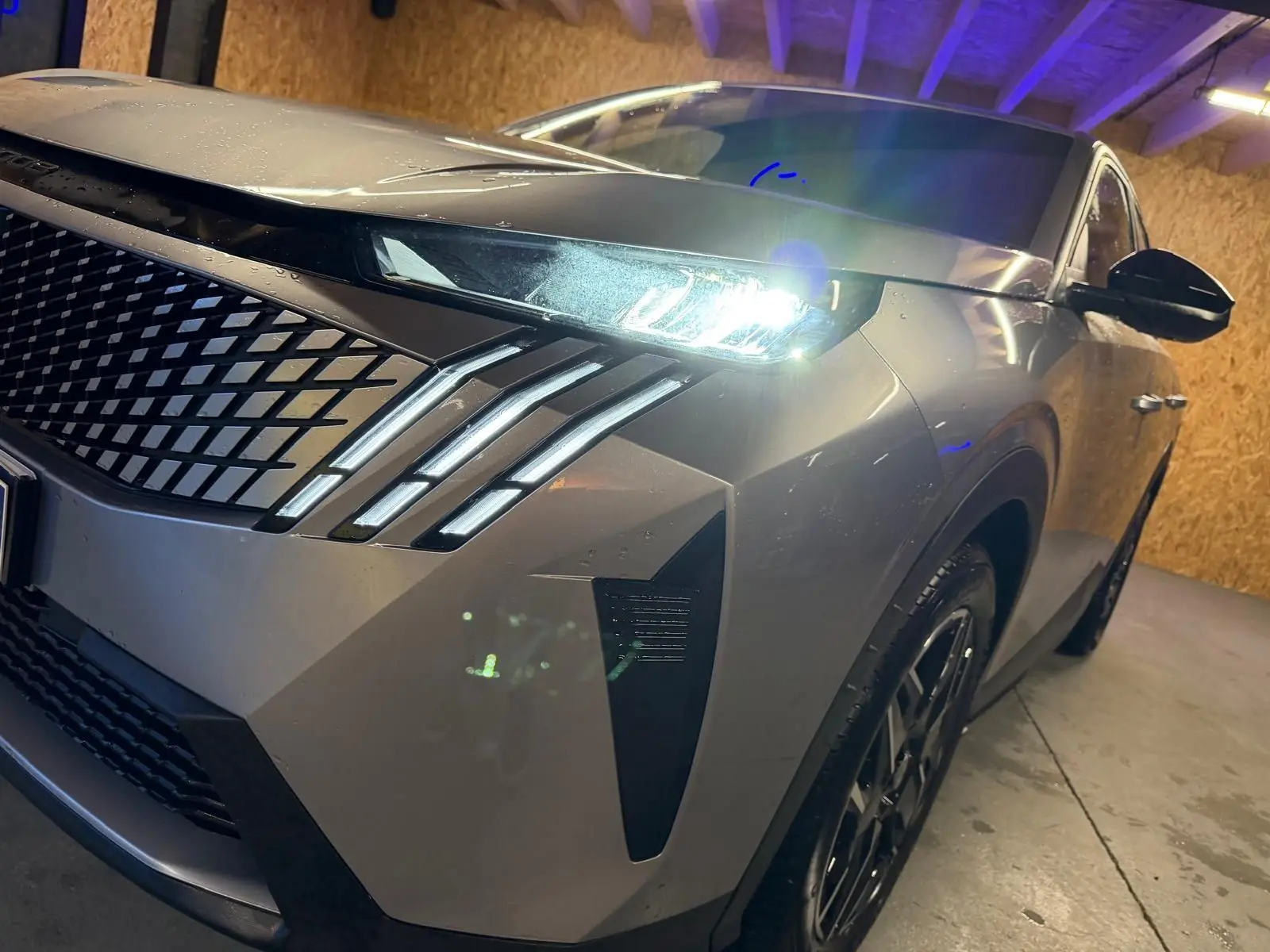 Vue 3/4 avant droit du Peugeot 3008 gris 2025 avec phares LED allumés et calandre distinctive en losanges.