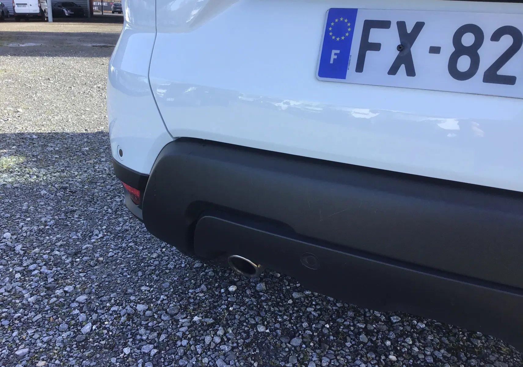 Vue rapprochée de l'arrière gauche d'un Dacia Duster blanc avec pare-chocs noir et sortie d'échappement visible.