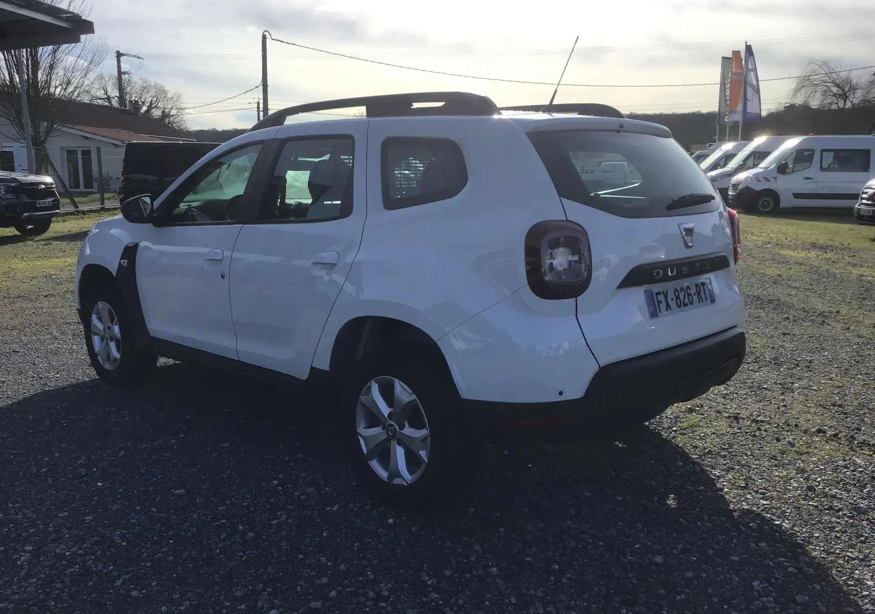 Vue 3/4 arrière droite d'un Dacia Duster blanc 2021 avec jantes alliage et grille de séparation visible à l'arrière.
