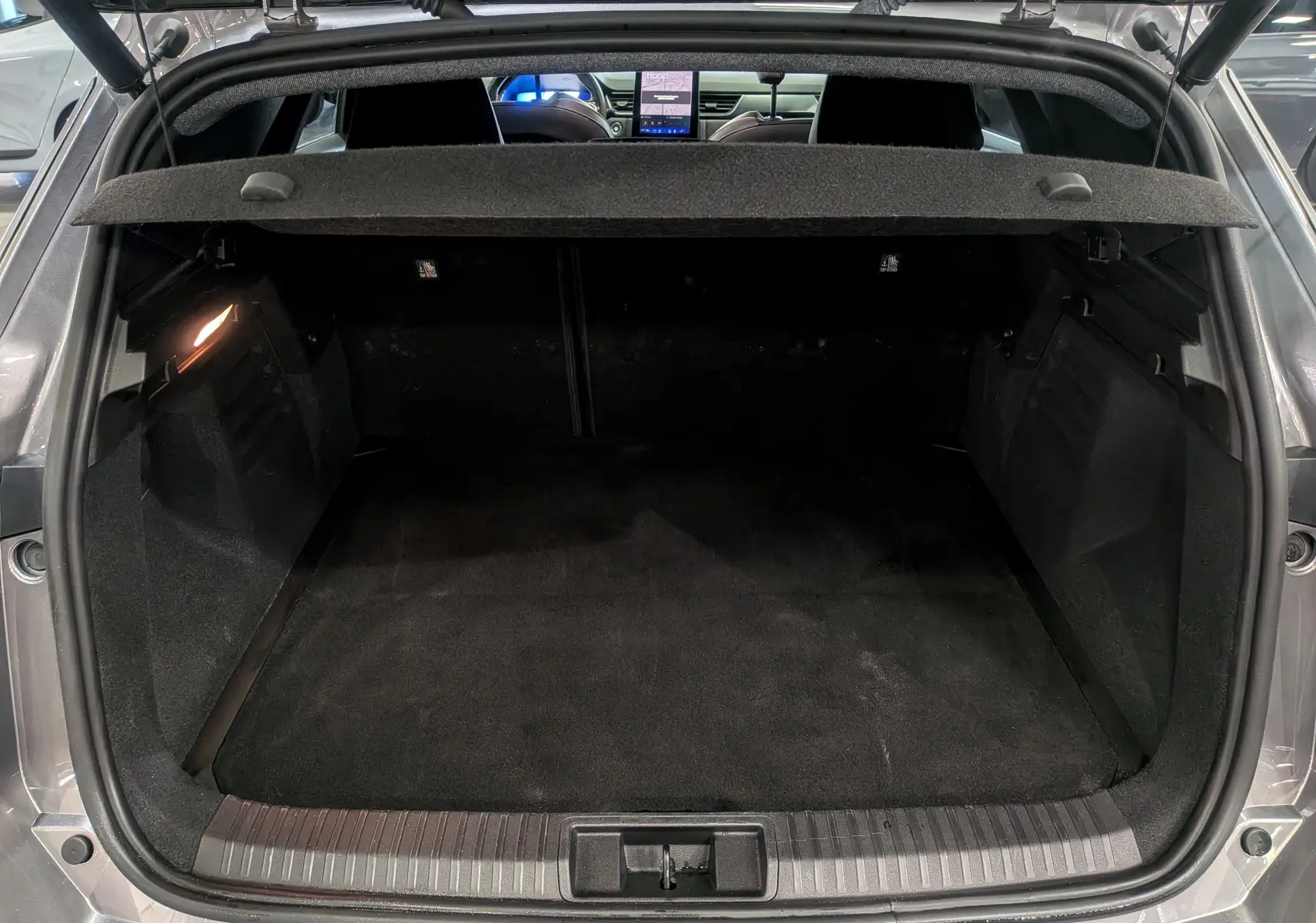 Coffre ouvert vu de l'arrière d'une Renault SYMBIOZ gris Cassiopé, avec intérieur noir et tablette arrière relevée.