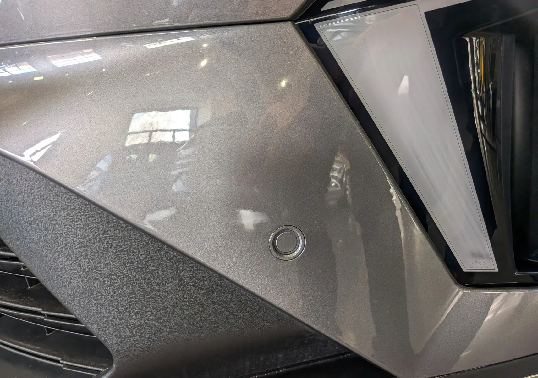 Gros plan sur le pare-chocs avant gris Cassiopé du Renault Symbioz E-TECH avec capteur de stationnement circulaire.