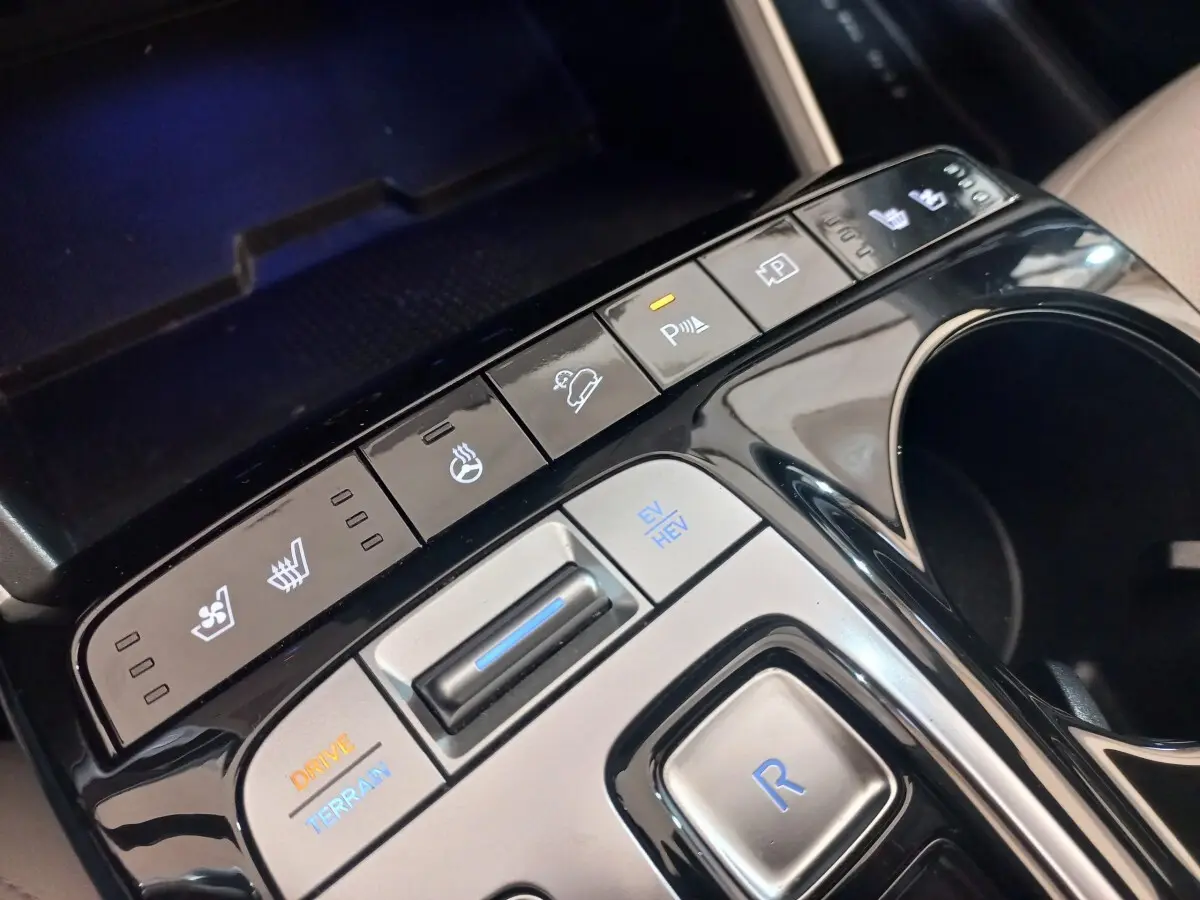 Gros plan sur la console centrale noire du Hyundai Tucson gris foncé, avec boutons de contrôle de conduite et sièges chauffants.