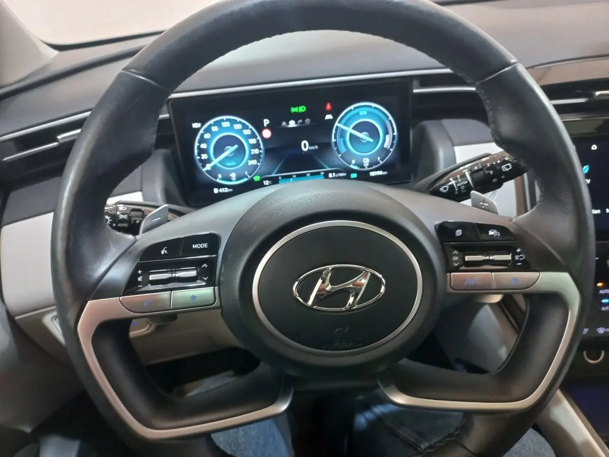Vue rapprochée du volant cuir et alu du Hyundai Tucson 2023 avec tableau de bord numérique lumineux.