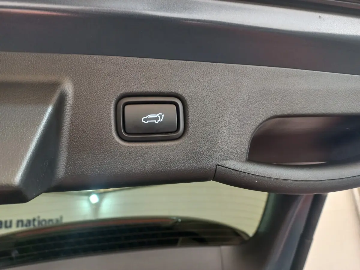 Gros plan sur le bouton d'ouverture électrique du coffre du Hyundai Tucson gris foncé, intérieur du hayon visible.