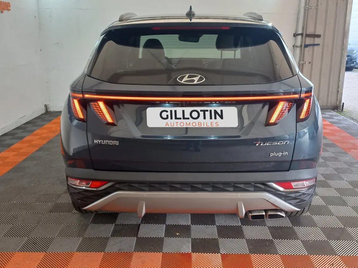 Vue arrière d'un Hyundai Tucson gris foncé 2023 avec feux LED allumés et double sortie d'échappement visible.