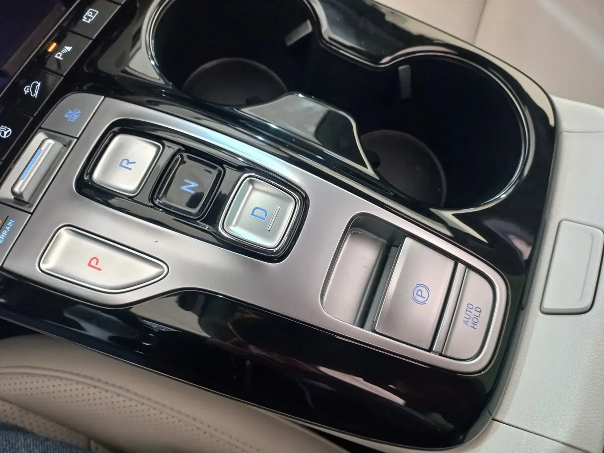 Gros plan sur la console centrale noire et argentée du Hyundai Tucson 2023, boutons de boîte auto et frein électrique visibles.