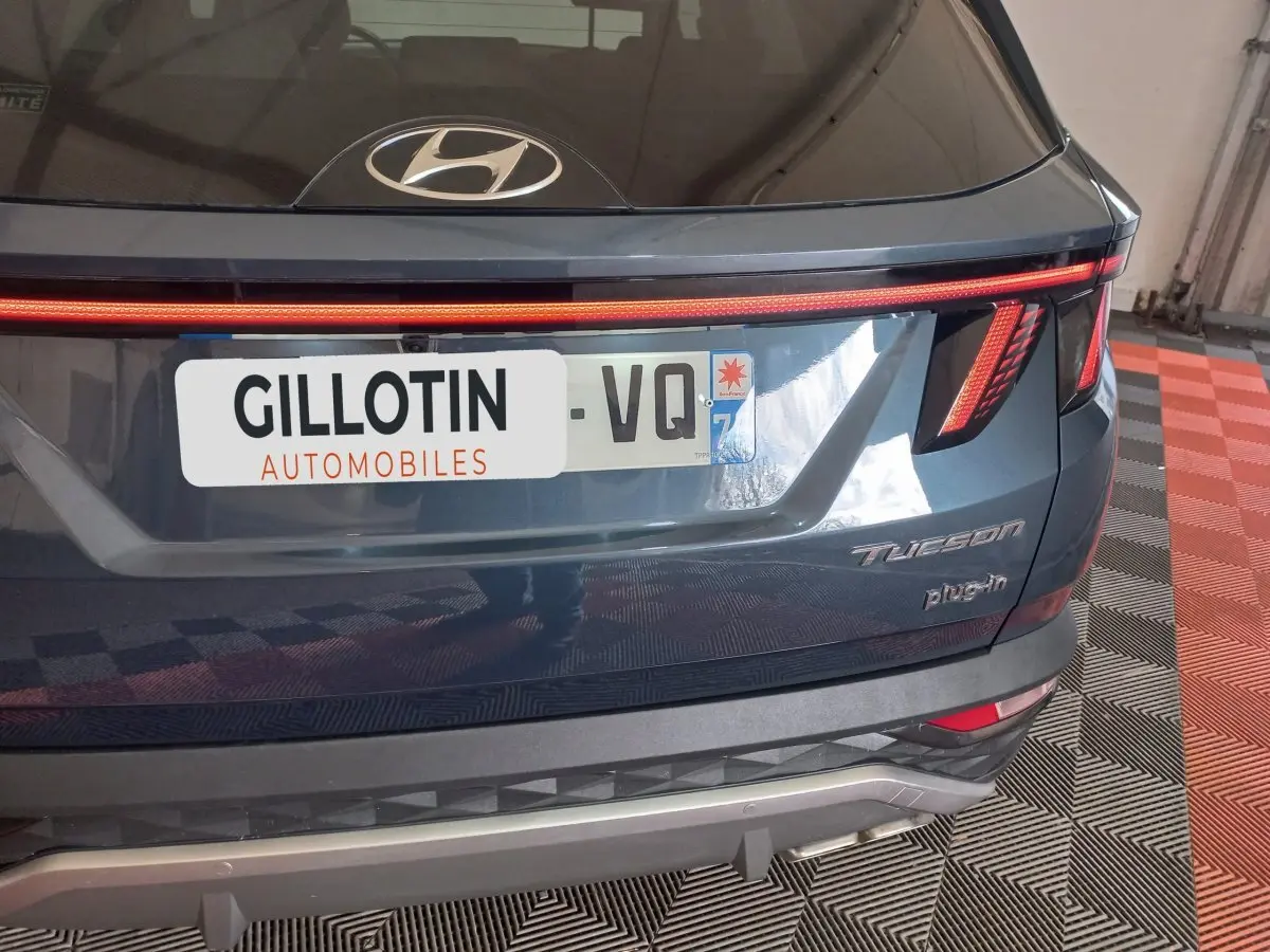 Vue arrière d’un Hyundai Tucson gris foncé 2023 avec feux LED et logo plug-in visible sur un sol à damier.