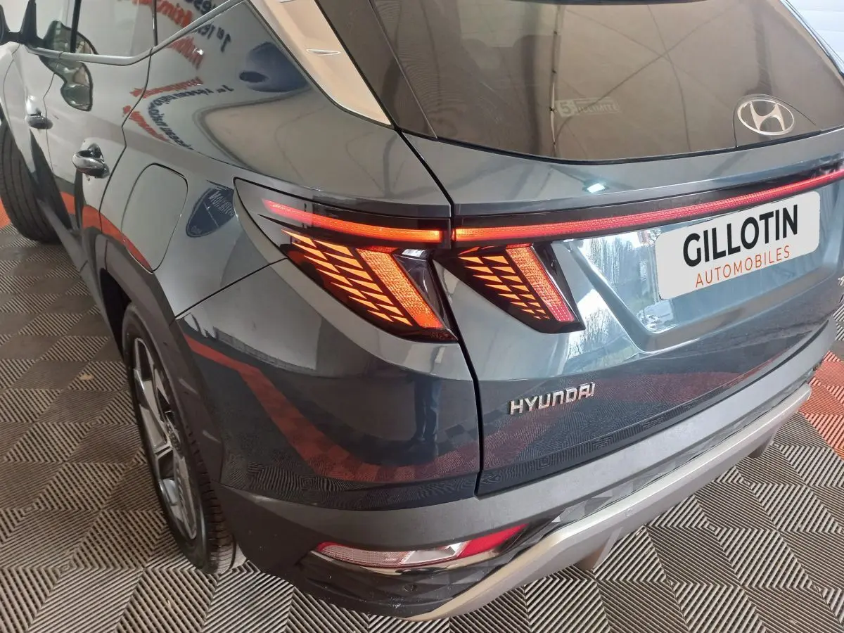 Vue 3/4 arrière gauche du Hyundai Tucson gris foncé avec feux arrière LED distinctifs allumés.