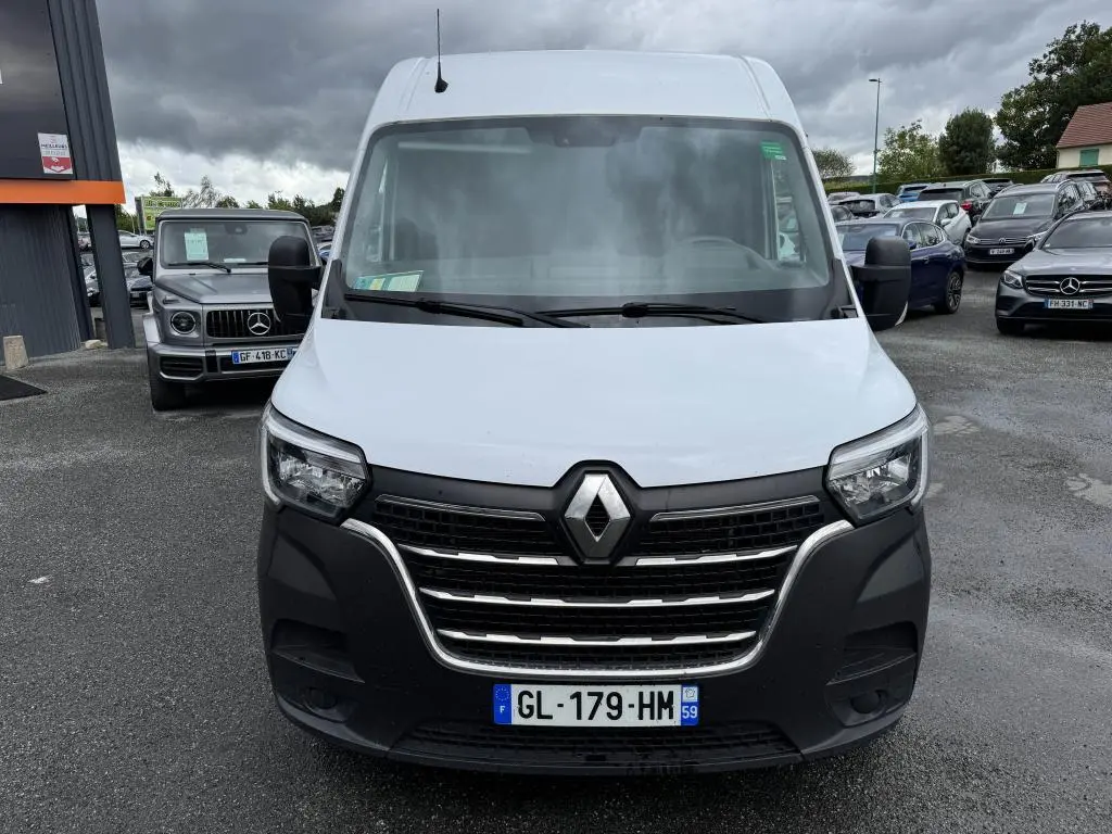 Renault Master blanc vu de face avec calandre noire et projecteurs antibrouillard sous un ciel nuageux.
