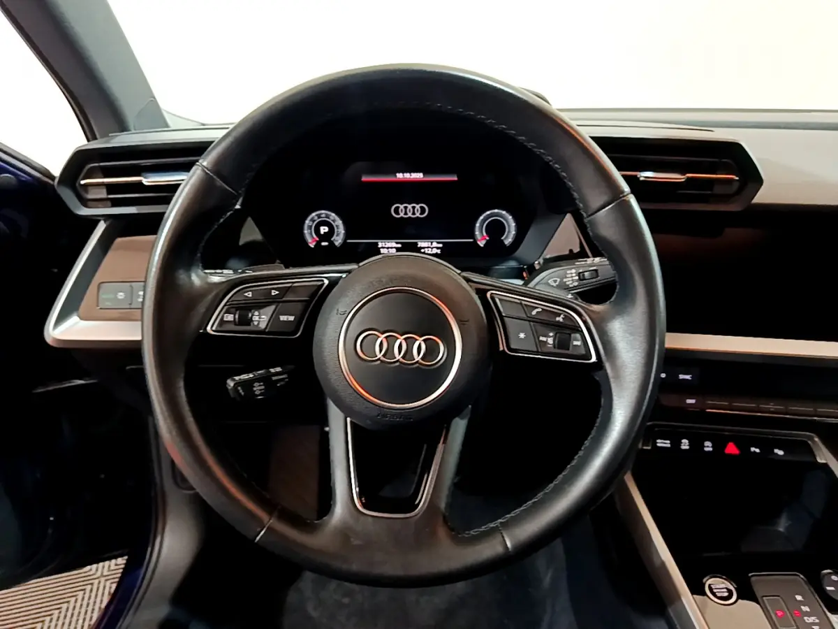 Vue centrée sur le volant cuir noir de l'Audi A3 35 TFSI 2023 avec tableau de bord numérique et détails intérieurs bleus.
