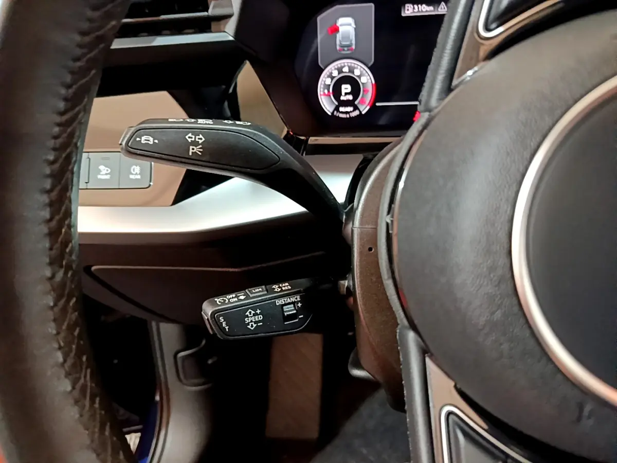 Gros plan sur la commande de régulateur de vitesse et levier de clignotant côté gauche du volant cuir d’une Audi A3 bleu 2023.