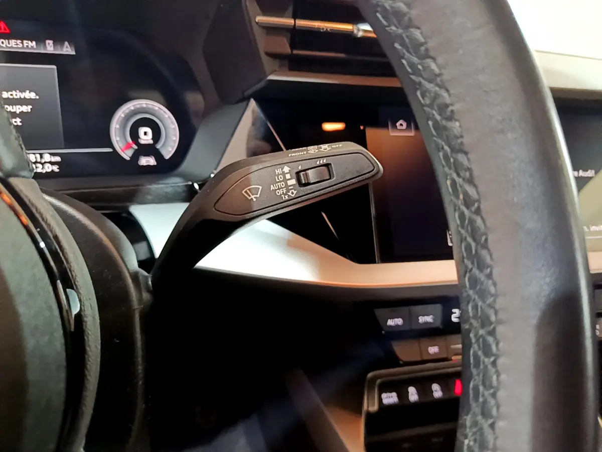 Gros plan sur la manette d’essuie-glace à gauche du volant cuir de l’Audi A3 bleu, avec tableau de bord numérique visible.