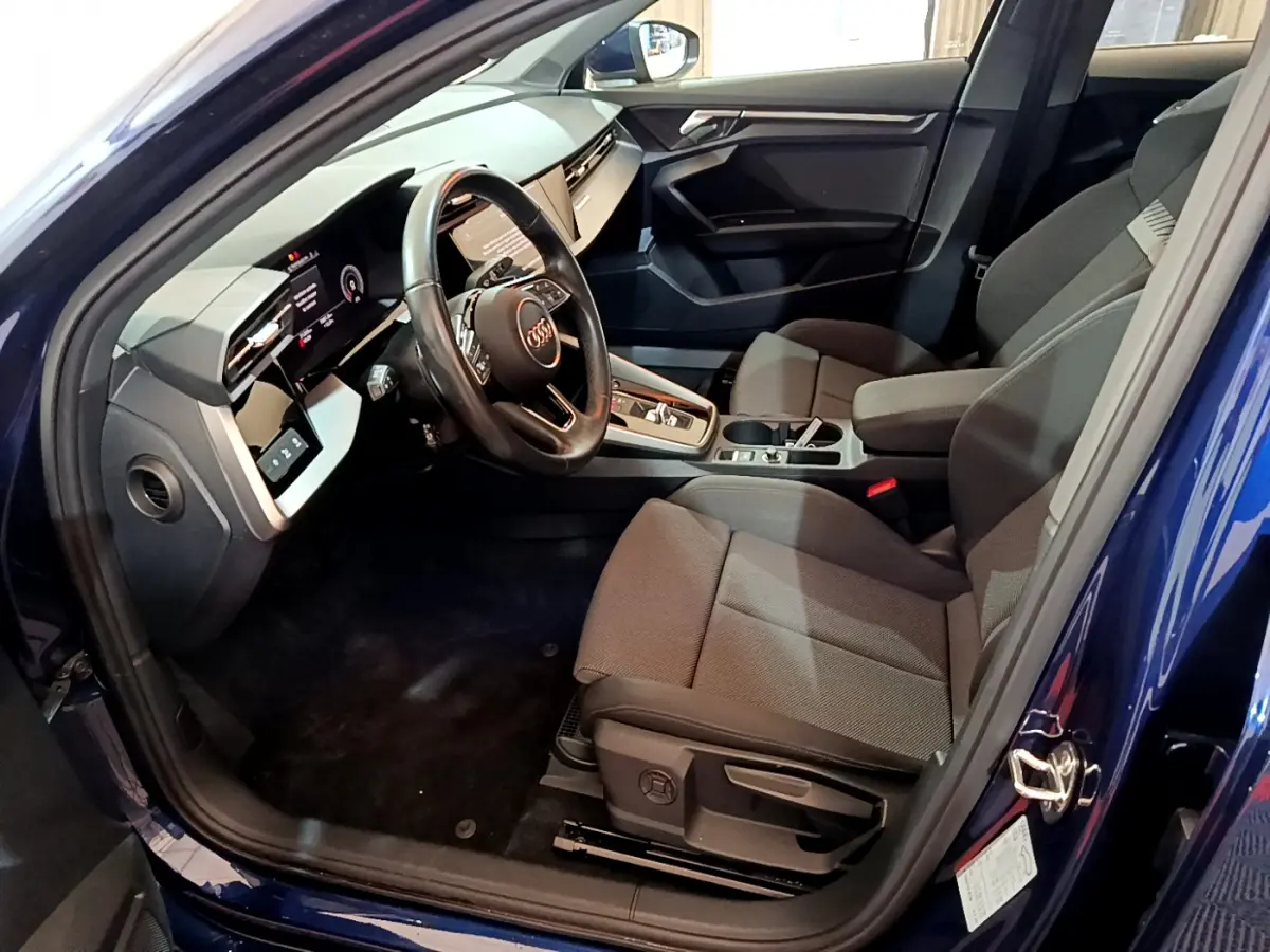 Intérieur côté conducteur d'une Audi A3 bleu 2023, volant cuir et tableau de bord numérique avec écran tactile.