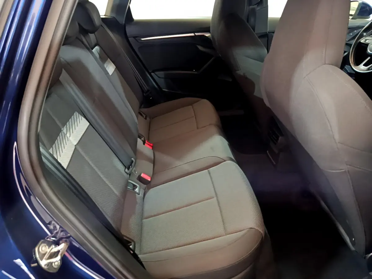 Vue intérieure côté gauche sur la banquette arrière grise d'une Audi A3 35 TFSI bleu 2023 avec portes ouvertes.
