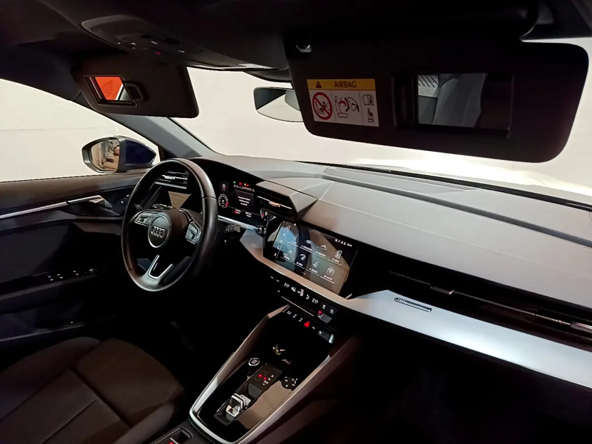 Intérieur de l'Audi A3 2023 vu côté conducteur, tableau de bord moderne avec écran tactile et volant cuir noir.