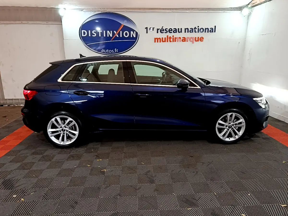 Profil latéral droit d'une Audi A3 35 TFSI bleu foncé, stationnée en intérieur sur sol carrelé gris et rouge.