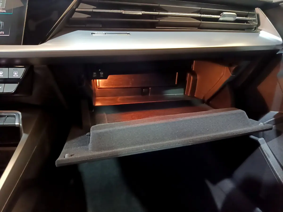 Ouverture de la boîte à gants éclairée côté passager dans l'habitacle noir de l'Audi A3 bleu 2023.