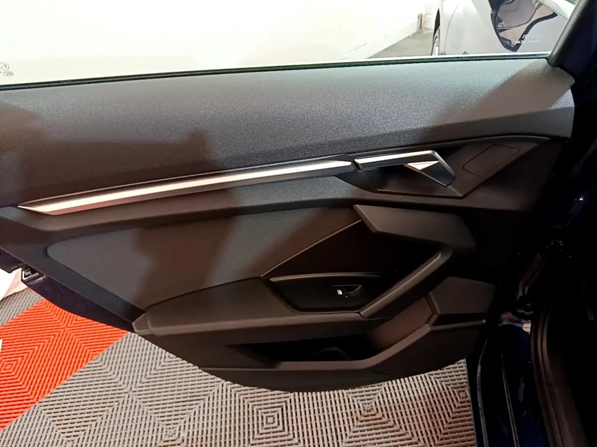 Vue intérieure côté gauche de la porte avant d'une Audi A3 35 TFSI bleu avec garniture noire et insert argenté.