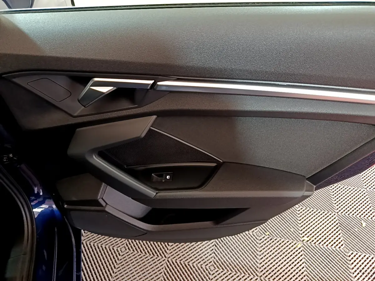 Gros plan sur la porte côté gauche bleu foncé d'une Audi A3 35 TFSI 150 MHEV avec poignée et commandes intégrées.
