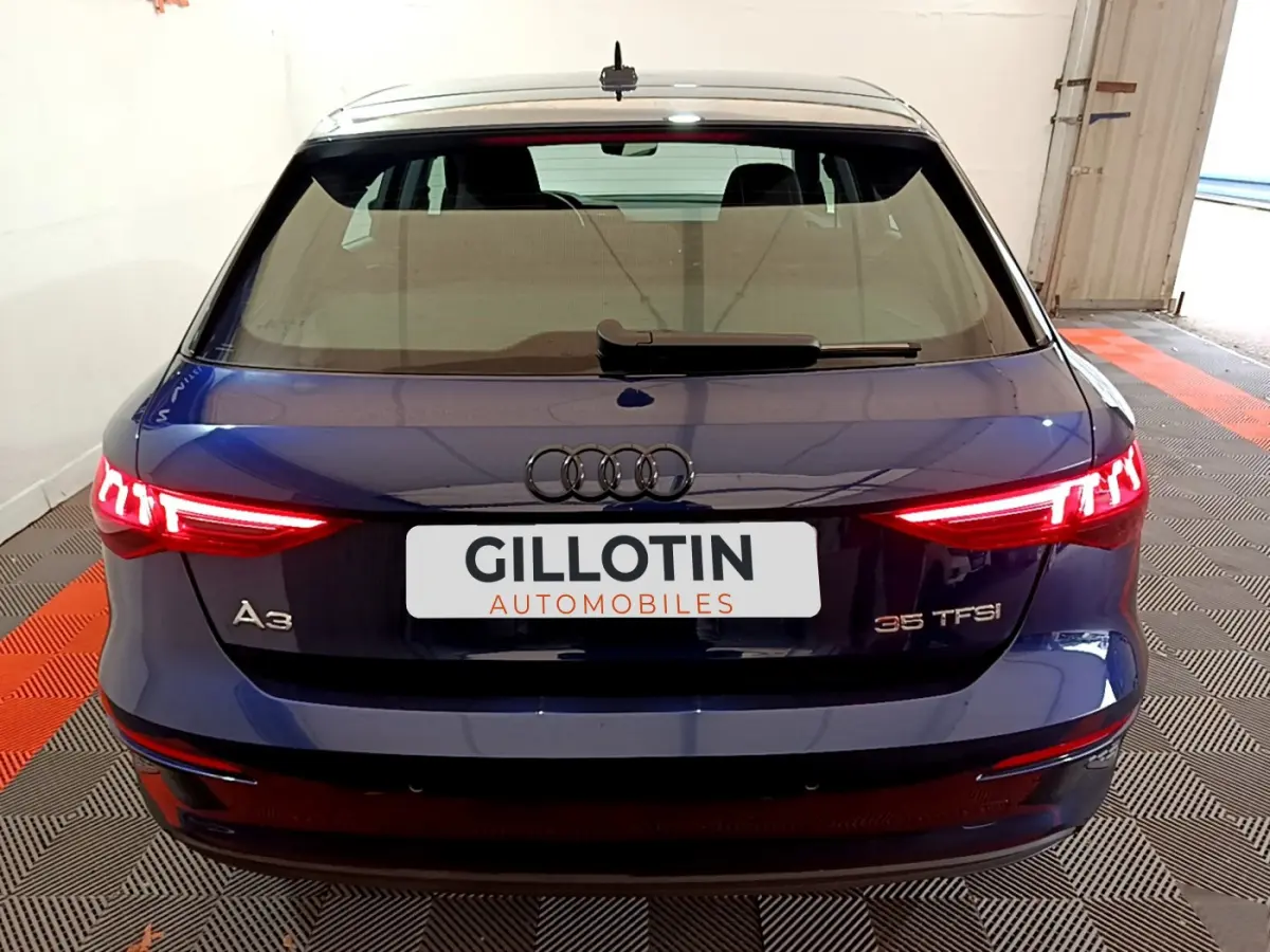 Vue arrière d'une Audi A3 35 TFSI bleu nuit avec feux arrière LED allumés dans un garage.