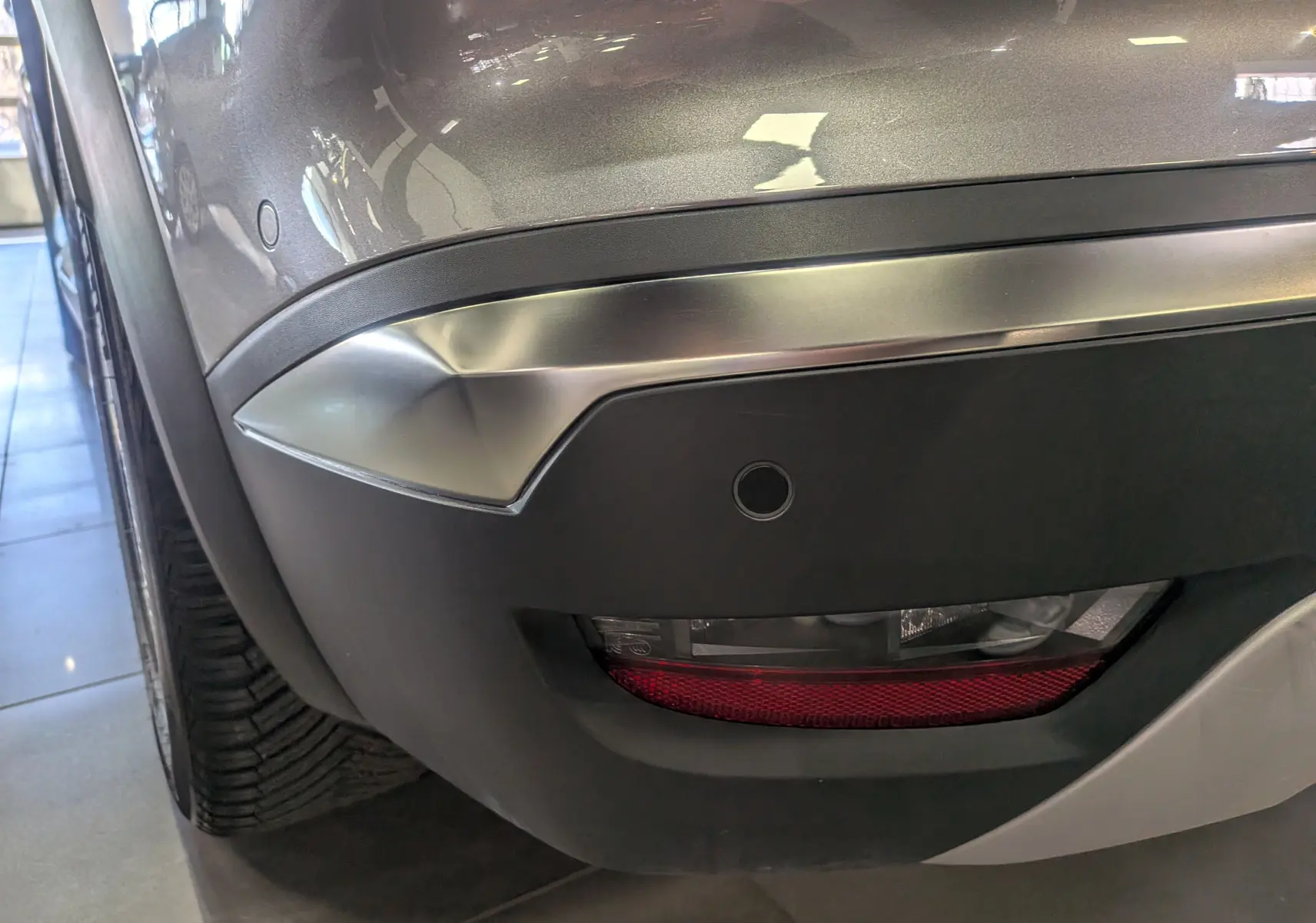 Gros plan sur le pare-chocs arrière droit gris Cassiopé du Renault Symbioz avec feu antibrouillard et capteur de recul.