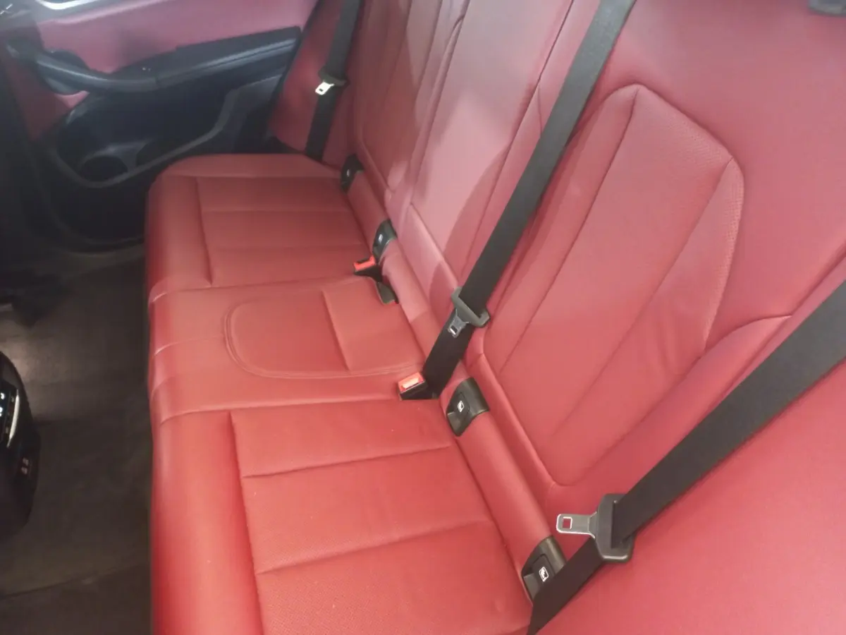 Vue rapprochée de la banquette arrière rouge avec ceintures noires du BMW X3 xDrive30e 2022 blanc.