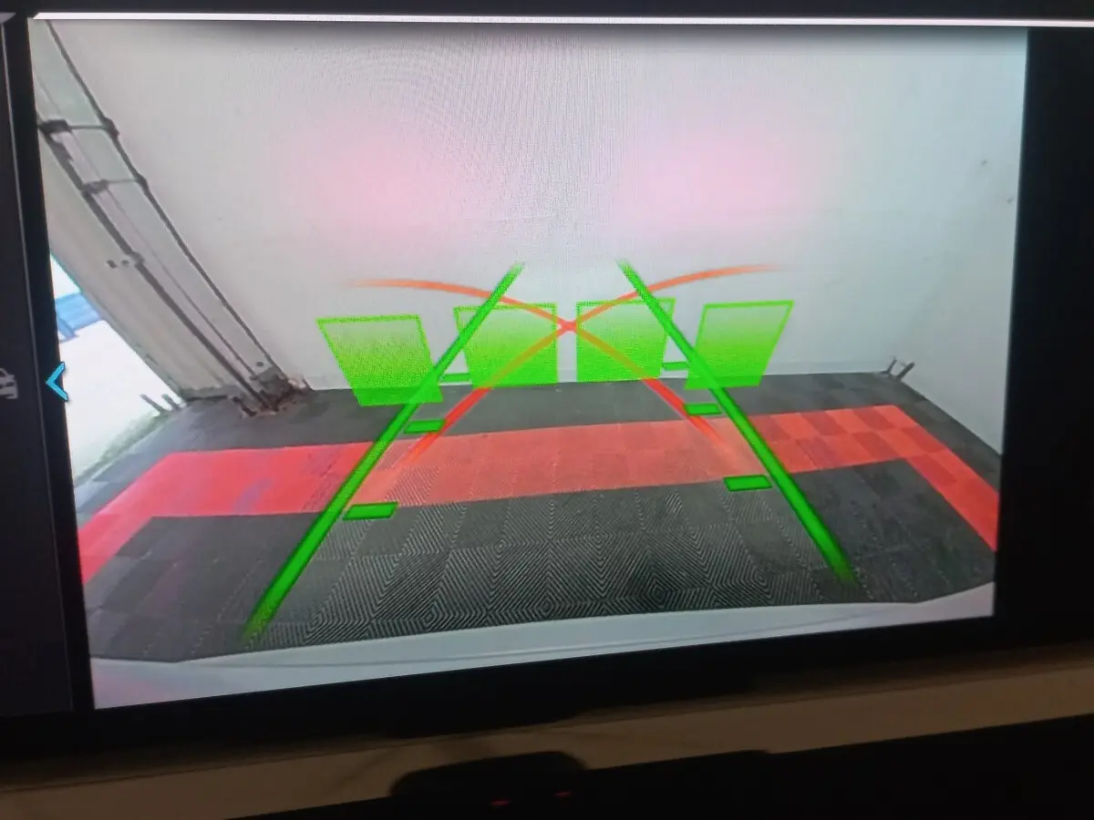 Vue caméra de recul du BMW X3 blanc xDrive30e montrant les lignes de guidage vertes et rouges au sol.