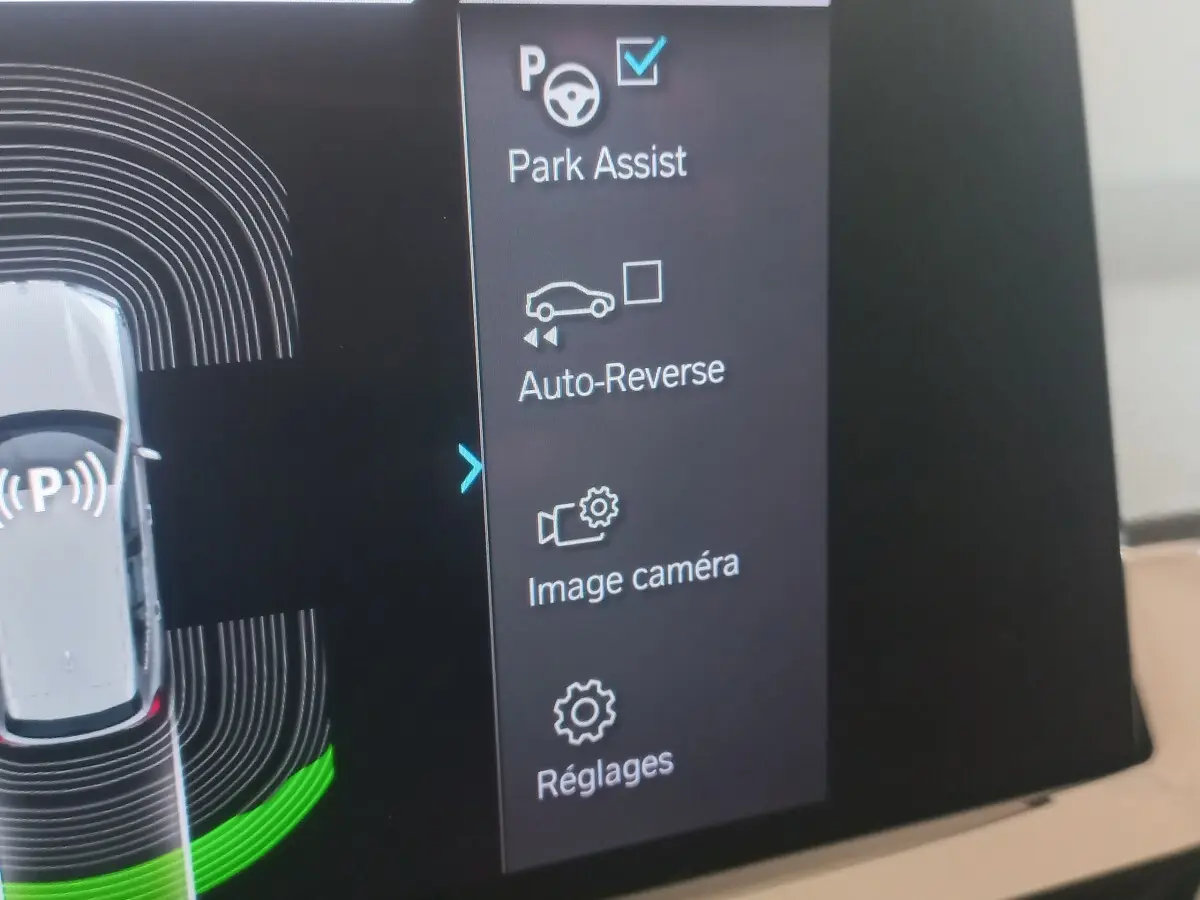 Écran tactile intérieur du BMW X3 blanc montrant les options d’aide au stationnement et caméra.
